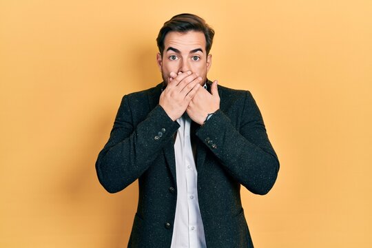 Handsome caucasian man with beard wearing elegant business jacket shocked covering mouth with hands for mistake. secret concept.