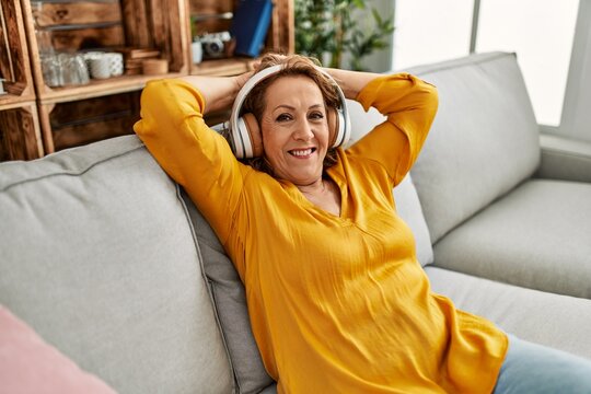 Middle age caucasian woman listening to music sitting on the sofa at home.