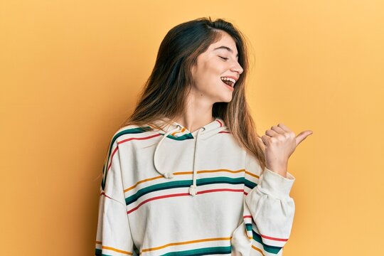 Young caucasian woman wearing casual clothes smiling with happy face looking and pointing to the side with thumb up.