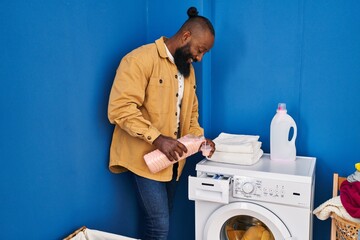 Young african american man smiling confident pouring detergent on washing machine at laundry room