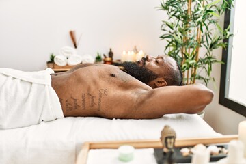 Obraz na płótnie Canvas Young african american man relaxed with hands on head lying on massage table at beauty center
