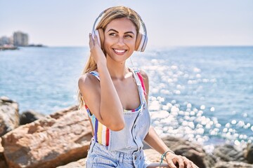 Young blonde girl listening to music sitting on the rock at the beach.