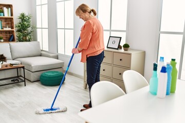 Middle age woman smiling happy washing floor at home.