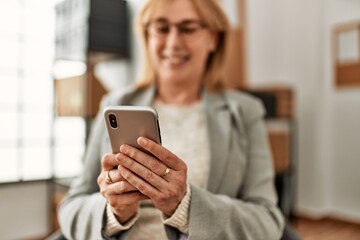 Middle age businesswoman smiling happy using smartphone at the office.