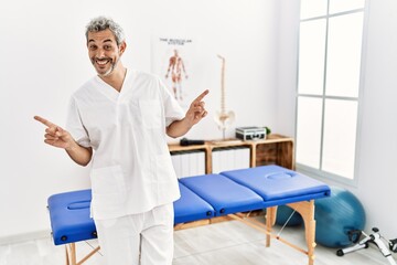 Fototapeta na wymiar Middle age hispanic therapist man working at pain recovery clinic smiling confident pointing with fingers to different directions. copy space for advertisement