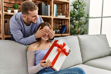 Young man surprising his girlfriend with birthday gift at home.