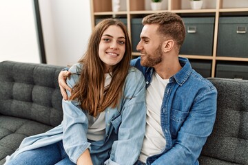 Young caucasian couple sitting on the sofa hugging at home.