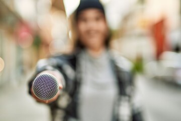 Young hispanic woman smiling happy using microphone at the city.