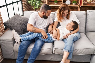 Family doing tickle to son sitting on sofa at home