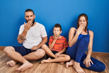 Family of three sitting on the floor at home bored yawning tired covering mouth with hand. restless...