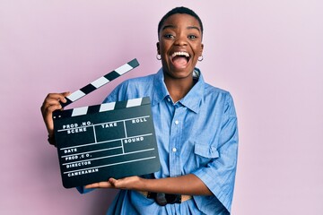 Young african american woman holding video film clapboard celebrating crazy and amazed for success with open eyes screaming excited.