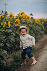 Little boy walks across a field of sunflowers in a hat and barefoot