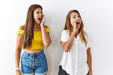 Mother and daughter together standing together over isolated background shouting and screaming loud to side with hand on mouth. communication concept.