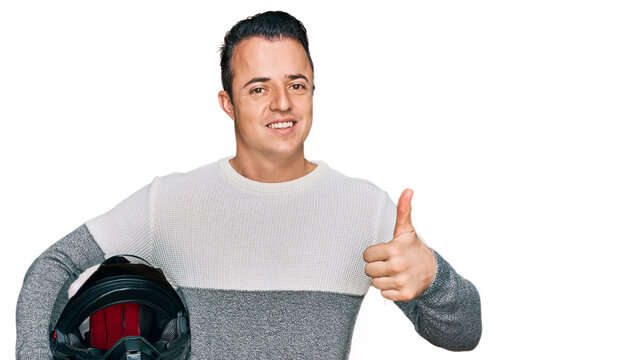 Handsome young man holding motorcycle helmet smiling happy and positive, thumb up doing excellent and approval sign