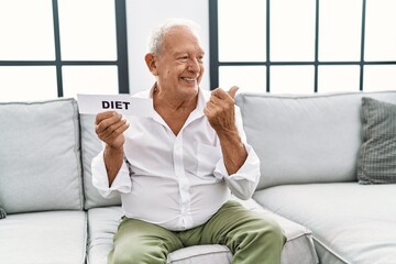 Senior man holding diet banner pointing thumb up to the side smiling happy with open mouth