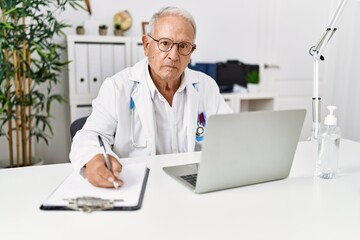 Naklejka na ściany i meble Senior man wearing doctor uniform writing on document working at clinic