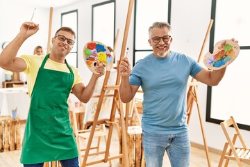 Group of middle age people drawing at art studio. Two students smiling happy holding paintbrush and...