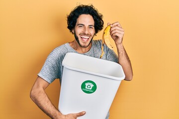 Handsome hispanic man recycling banana peel composting organic fertilizer celebrating crazy and...