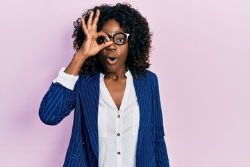 Young african american woman wearing business clothes and glasses doing ok gesture shocked with surprised face, eye looking through fingers. unbelieving expression.