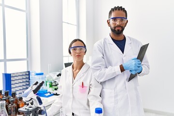 Man and woman scientist partners holding clipboard looking to the camera at laboratory