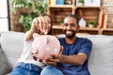 Man and woman couple smiling confident insert coin on piggy bank at home