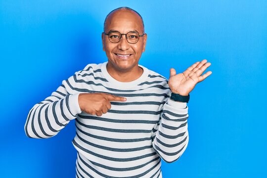 Middle age latin man wearing casual clothes and glasses amazed and smiling to the camera while presenting with hand and pointing with finger.