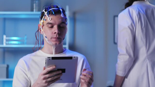 Man wearing EEG topographer for examining brain, doctor making electrogram of scalp activity. Researching of brain work using electroencephalography headset.