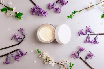 Cosmetic cream in a jar and spring blossom on light gray background. Natural cosmetics concept. Top view, flat lay