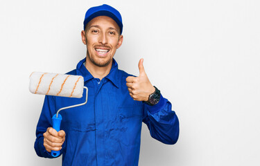 Bald man with beard holding roller painter smiling happy and positive, thumb up doing excellent and...