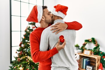 Two hispanic men couple surprise with engagement ring standing by christmas tree at home
