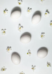 White spring flowers and eggs on white background. Minimalistic Easter concept. Creative holiday inspiration.