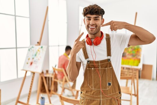 Young hispanic man at art studio smiling cheerful showing and pointing with fingers teeth and mouth. dental health concept.