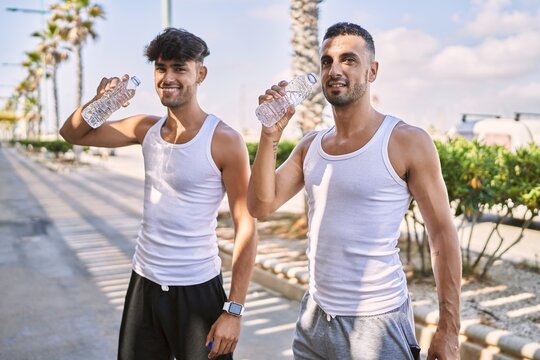 Two hispanic men sporty couple smiling confident drinking water at street