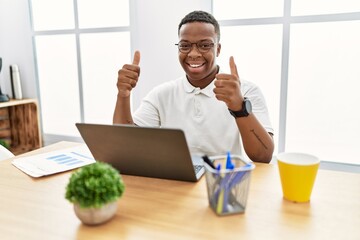 Young african man working at the office using computer laptop success sign doing positive gesture...