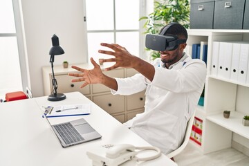 Young african american man wearing doctor uniform using virtual reality glasses at clinic