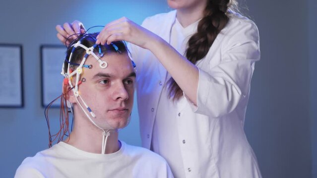 Man wearing EEG topographer for examining brain, doctor making electrogram of scalp activity. Researching of brain work using electroencephalography headset.