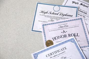 A honor roll recognition, certificate of achievement and high school diploma lies on table. Education documents