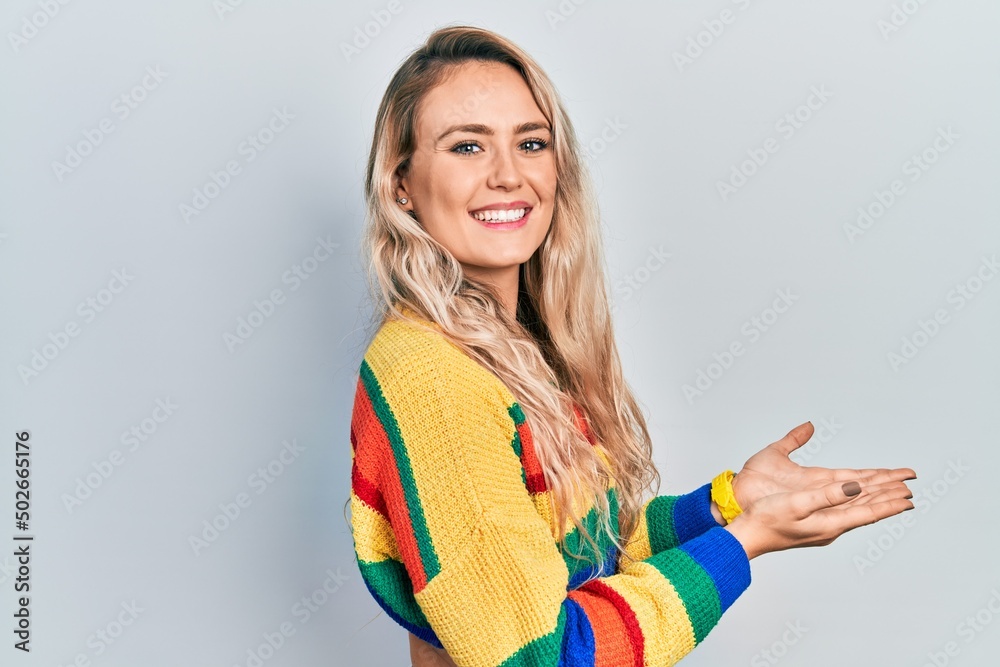 Wall mural beautiful young blonde woman wearing colored sweater pointing aside with hands open palms showing co