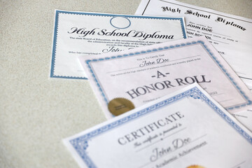 A honor roll recognition, certificate of achievement and high school diploma lies on table....