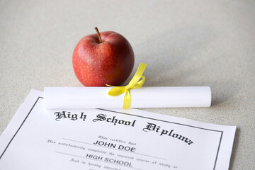 A high school diploma lies on table with small scroll and red apple. Education documents