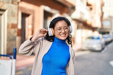 Young chinese woman smiling confident listening to music at street