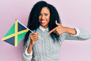 Middle age african american woman holding jamaica flag smiling happy pointing with hand and finger