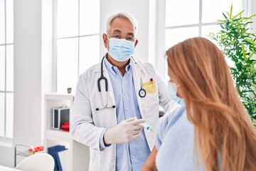 Fototapeta premium Middle age man and woman doctor wearing medical mask vaccinating patient at clinic