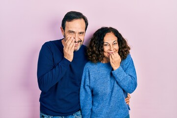 Middle age couple of hispanic woman and man hugging and standing together laughing and embarrassed...