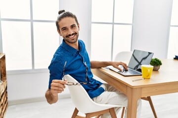 Obraz premium Handsome hispanic man working with laptop wearing glasses at the office