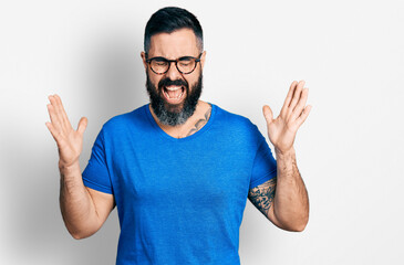 Naklejka premium Hispanic man with beard wearing casual t shirt and glasses celebrating mad and crazy for success with arms raised and closed eyes screaming excited. winner concept