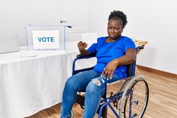 Young african woman sitting on wheelchair voting putting envelop in ballot box depressed and worry for distress, crying angry and afraid. sad expression.