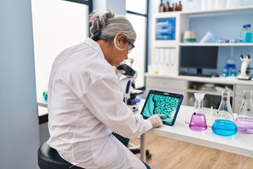 Fototapeta na wymiar Middle age woman wearing scientist uniform watching embryo on touchpad at laboratory