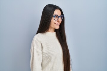 Young hispanic woman wearing casual sweater over blue background looking to side, relax profile pose with natural face with confident smile.