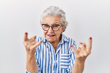 Senior woman with grey hair standing over white background shouting with crazy expression doing rock symbol with hands up. music star. heavy concept.